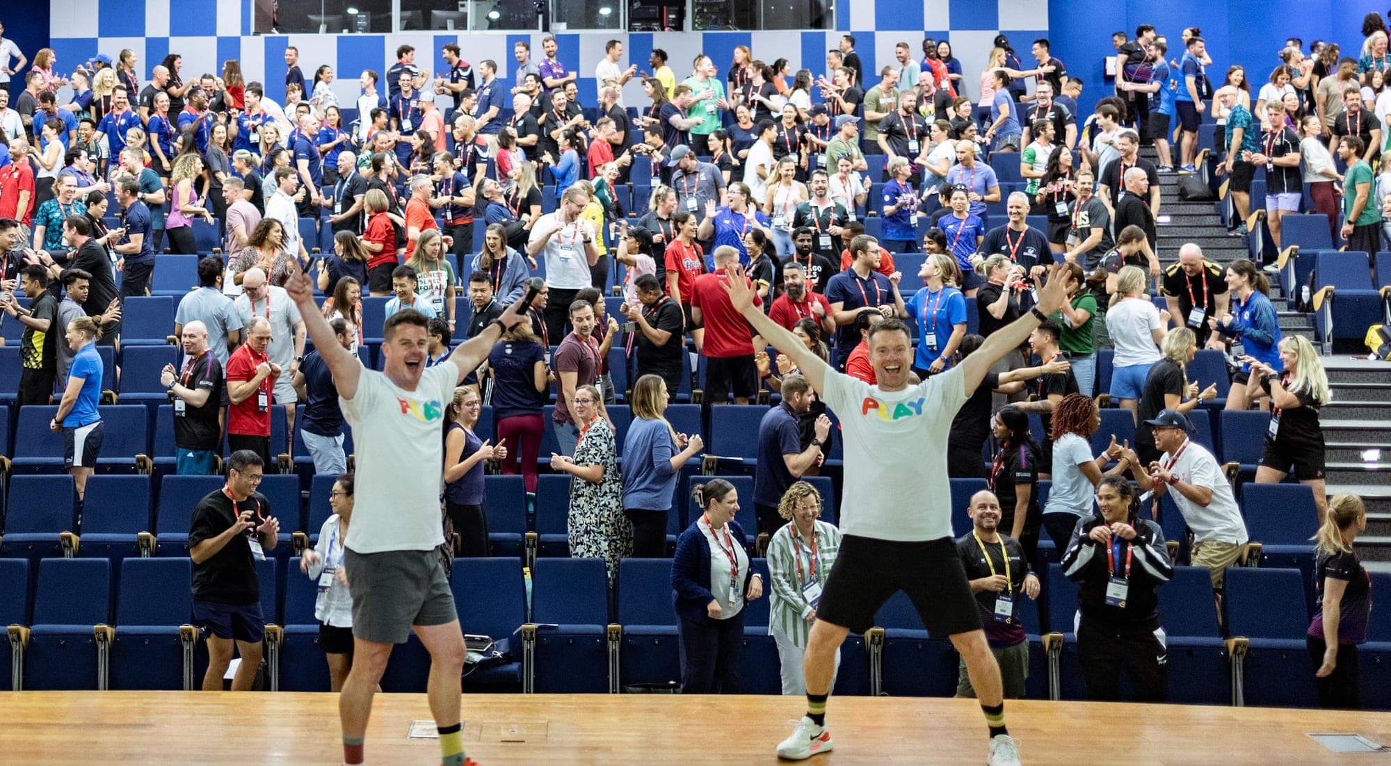 Two School of Play presenters on stage, arms raised, in front of an auditorium of educators on their feet