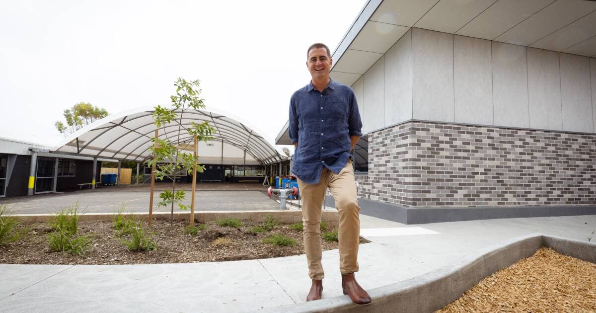 Simon Perry smiling outside a school building, beside a covered play area